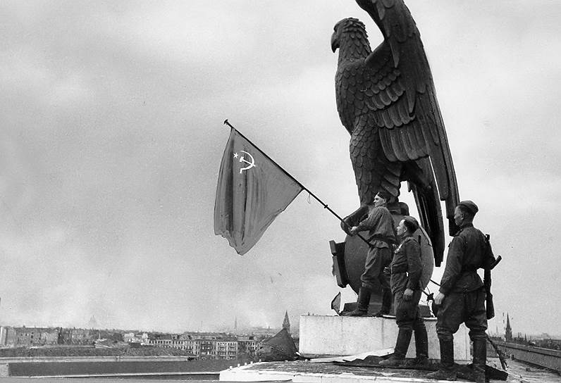 Германия. Берлин. Бойцы Красной Армии с советским флагом на крыше здания аэропорта Темпельхоф после взятия города в ходе Второй мировой войны. Евгений Халдей/ТАСС. https://www.gazeta.ru/army/photo/yevgeny-khaldei-best-photos.shtml?p=main&photo_num=11