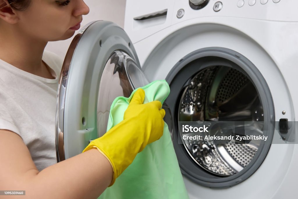 Женщина протирает дверцу стиральной машины, демонстрируя заботу о чистоте техники.