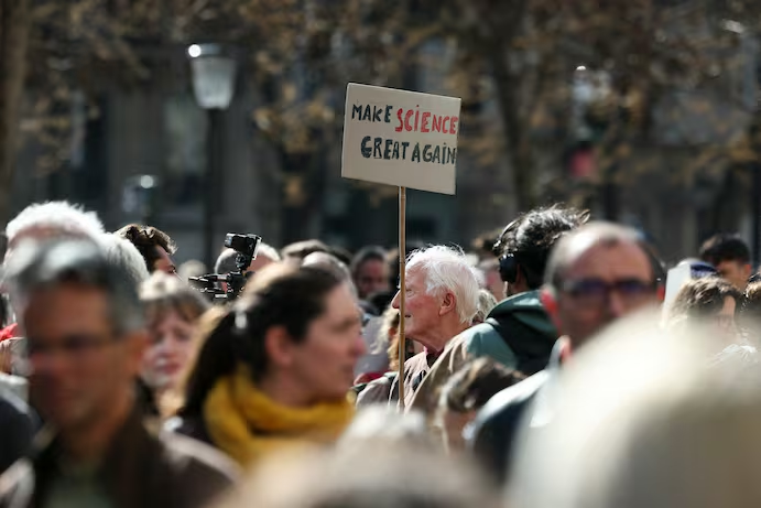 Фрэнсис Ронделез, почетный директор по научным исследованиям, держит плакат во время демонстрации в поддержку американских ученых в Париже 3 апреля. (Ален Жокар/AFP/Getty Images).