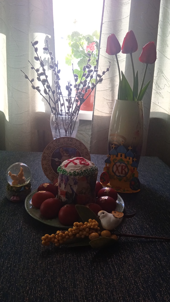 Мой стол. Герань на окошке расцвела к празднику. На часах, которые под вербочкой картина Кустодиева с пасхальной тематикой. Мы их купили в музее Кустодиева в Астрахани. 