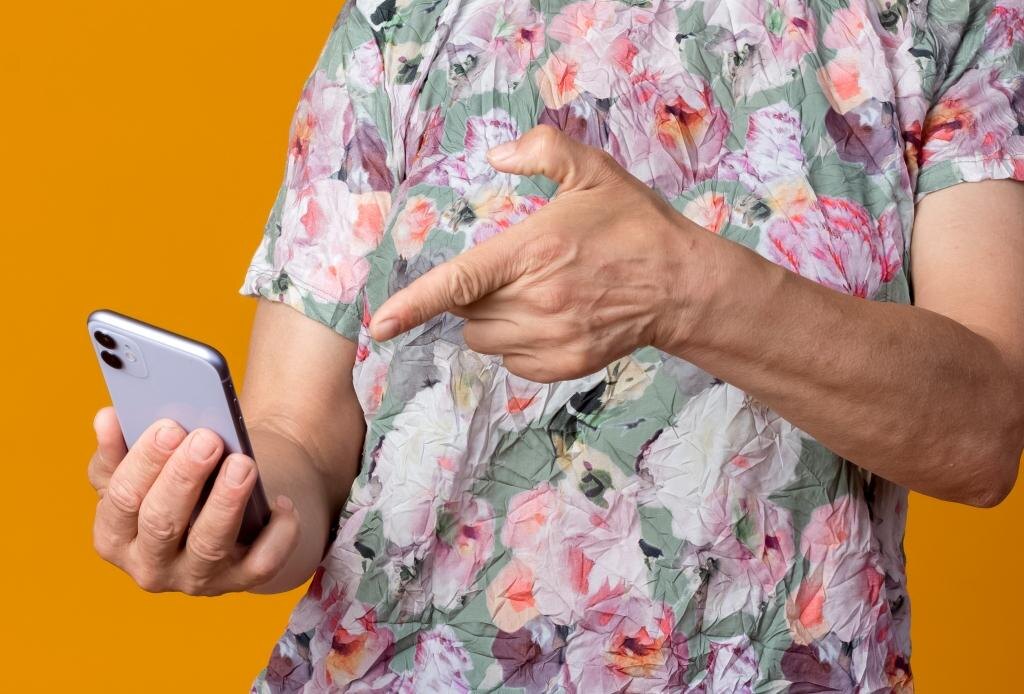    annoyed elderly woman holds and points at phone isolated on orange background with copy space Оксана Колесова