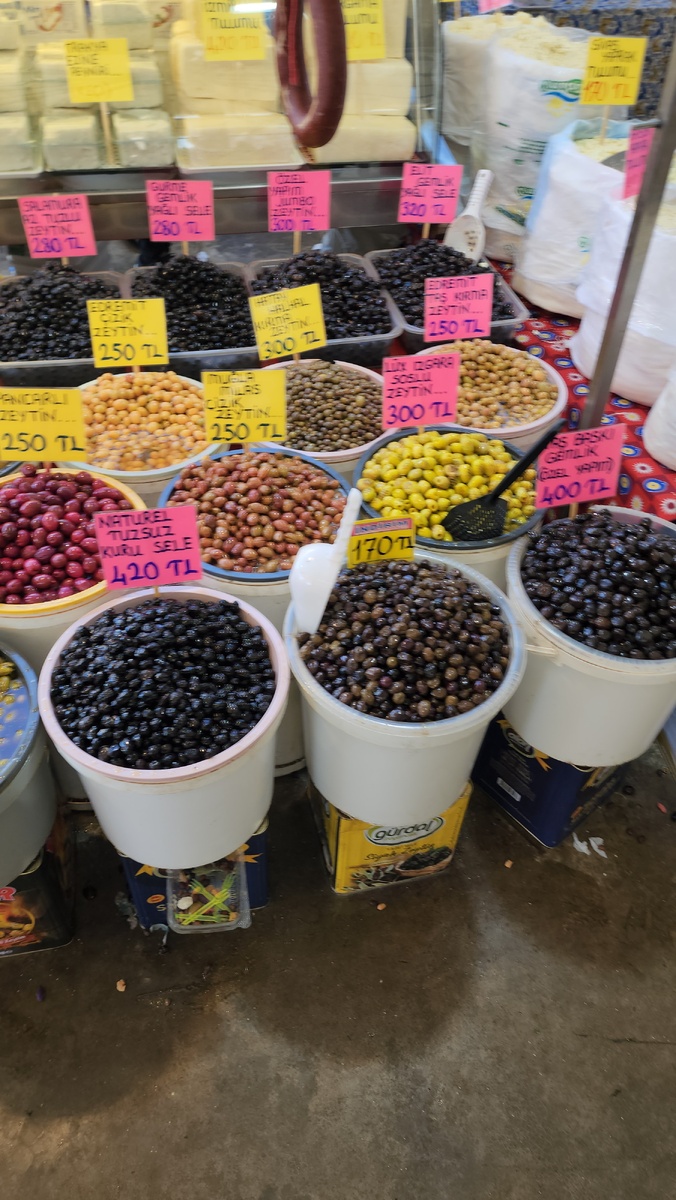 Цены на оливки на базаре. Эти большие вёдра стоят на металлических банках, заводских банках, из которых высыпали в а-ля домашнюю тару