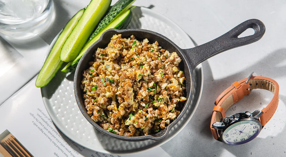 Готовое блюдо: рассыпчатая гречка с яйцом и луком, поданная прямо в сковороде.