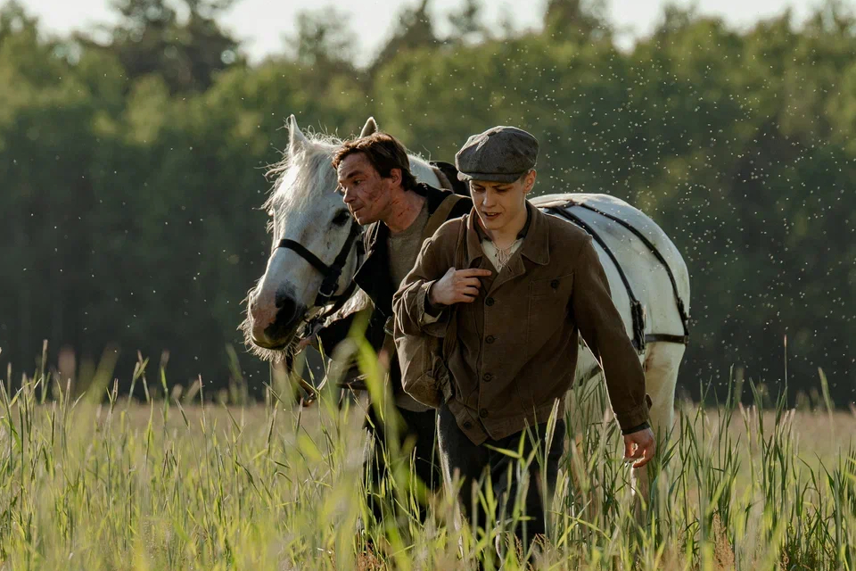 Кадр из фильма Почтарь (2025): Александр Петров (Почтарь) и молодой актер с лошадью идут по летнему полю