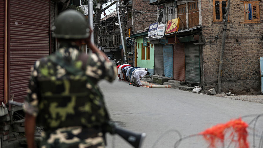 Солдат индийской военизированной организации стоит на страже, пока кашмирские мусульмане проводят пятничные молитвы во время комендантского часа у местной мечети в Сринагаре, 16 августа 2019 года / Mukhtar Khan/AP 