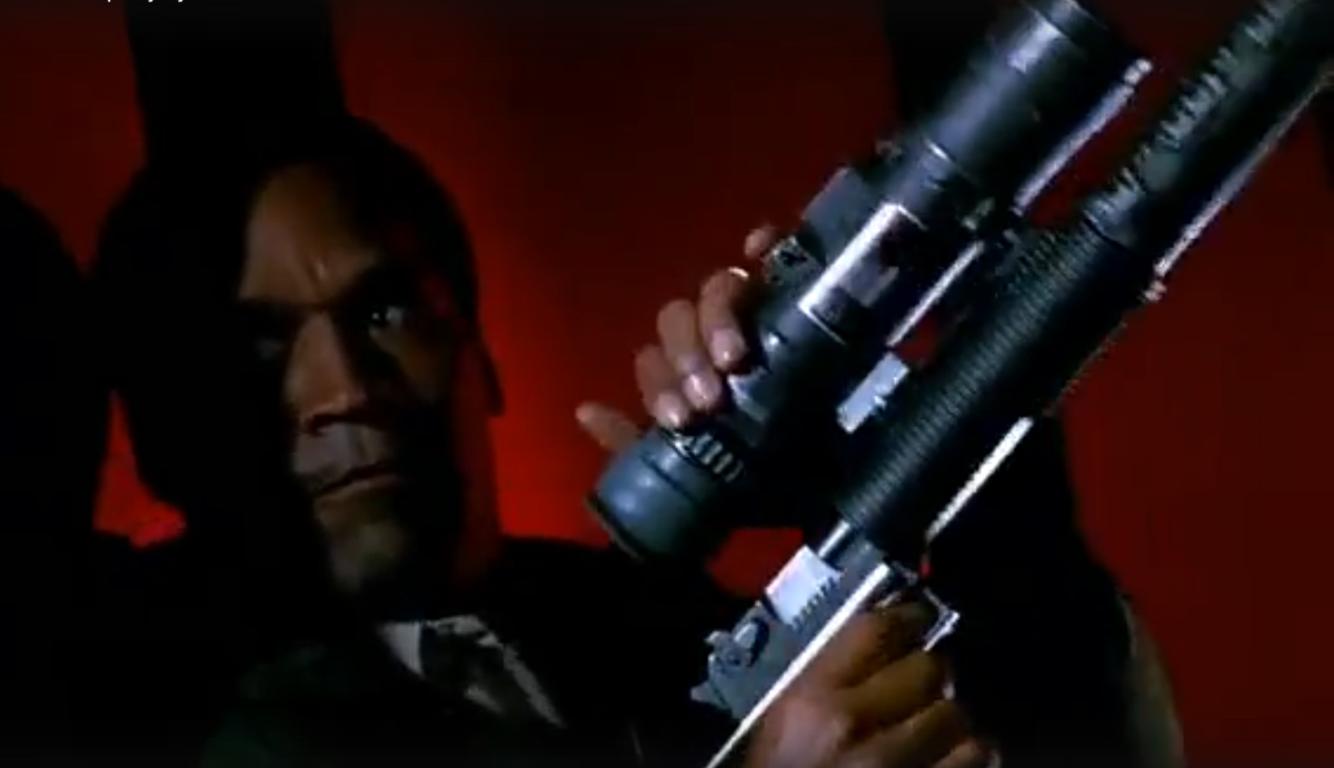 Кадр из фильма "Голый пистолет", на котором детектив Нордберг во время перестрелки на крыше из своего "Desert Eagle" собирает зенитку.