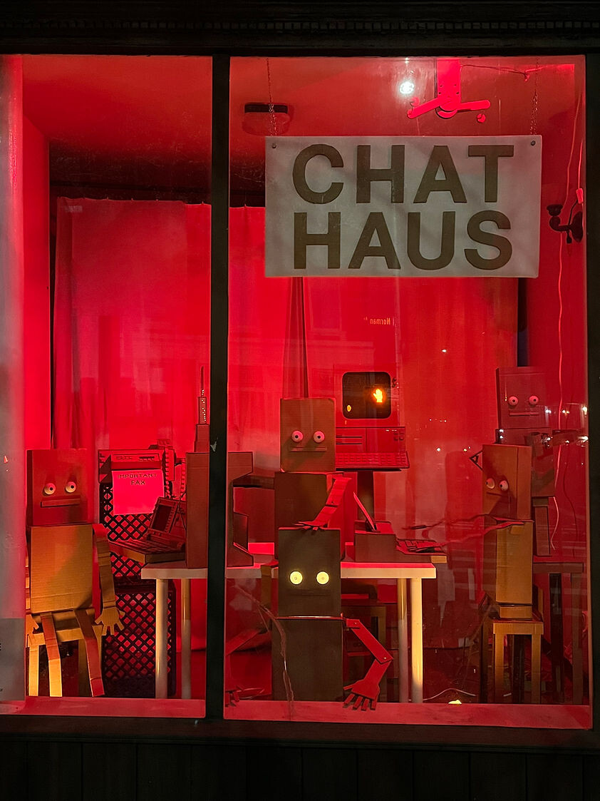 Фото витрины Chat Haus с картонными фигурами ботов за ноутбуками и надписью «CHAT HAUS»