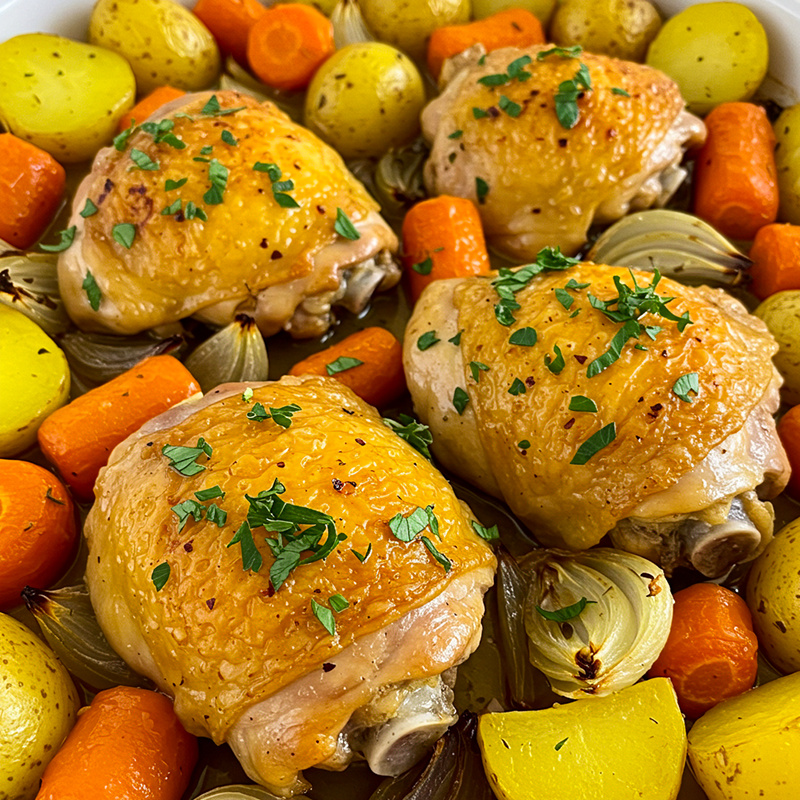 Аппетитная золотистая курица с запеченными до мягкости картофелем, морковью и луком, посыпанная свежей зеленью.