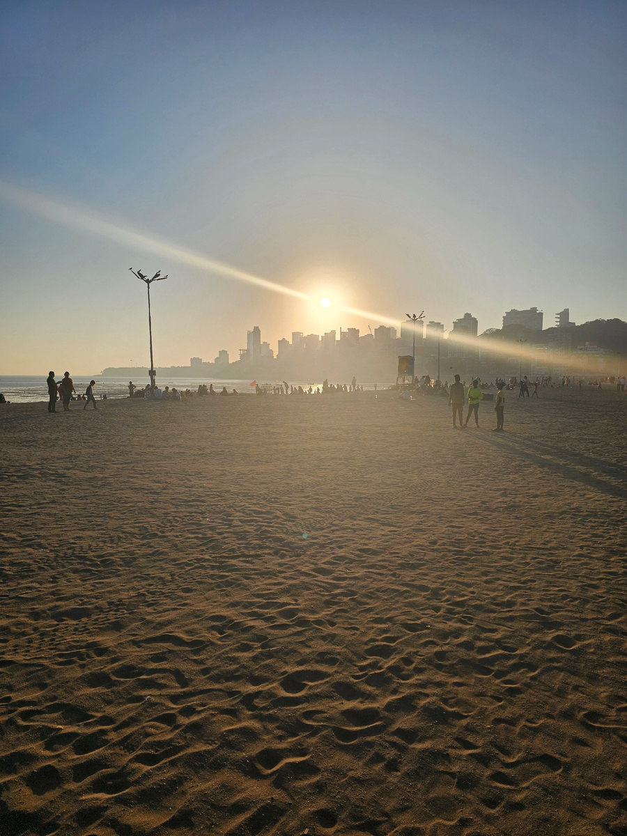 Мумбаи провожает день у Аравийского моря, где силуэты небоскребов растворяются в золотом тумане, а последние лучи солнца превращают волны в жидкое серебро. На пляже — вся эта удивительная смесь: студенты с селфи-палками рядом с семьями в традиционных сари, айтишники в беговых кроссовках бок о бок с местными рыбаками. Закат — это часы вздоха города, когда люди всех слоев общества приходят сюда, чтобы просто быть рядом с океаном и на миг забыть о городской суматохе.
