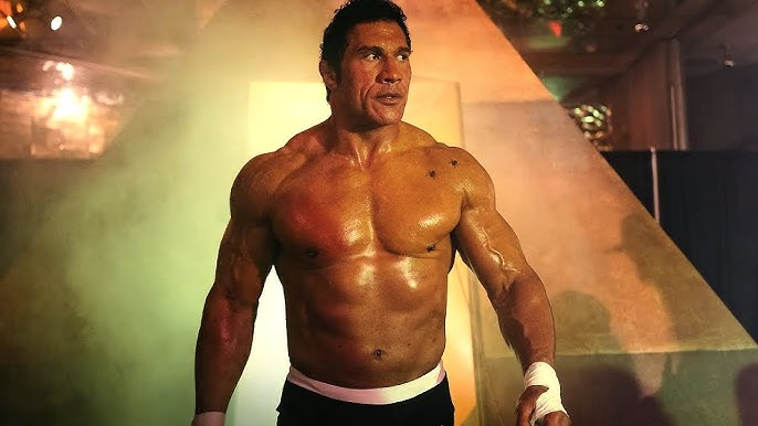 Дуэйн Джонсон в роли Марка Керра в фильме Крушащая машина, мускулистый, без рубашки, с обмотанными руками, выходит из тумана на арену