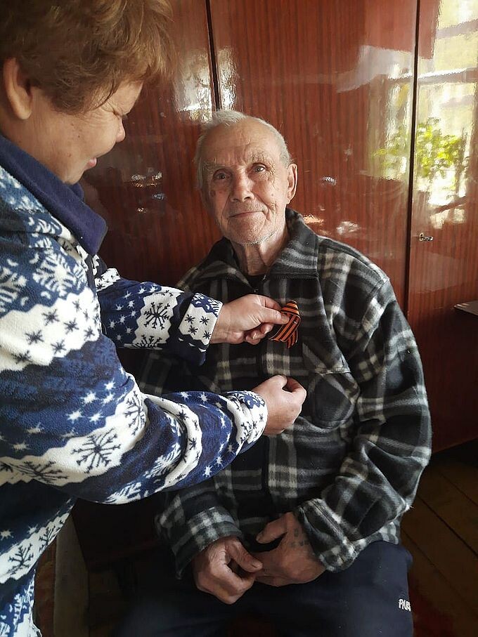 Соцработница прикрепляет Георгиевскую ленточку пожилому мужчине