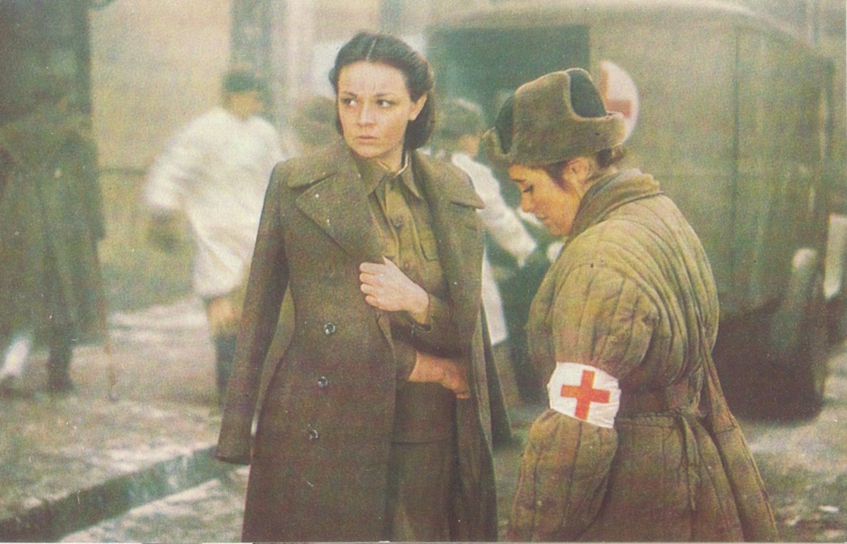 Открытка иллюстрированная. Кадр из фильма «Блокада». На лицевой стороне горизонтальное полноформатное фотографическое изображение. Кадр из фильма-эпопеи «Блокада» по одноименному роману Александра Чаковского. Слева актриса Ирина Акулова в роли Веры Королёвой. На оборотной стороне: отсутствует почтовое графление, в правом верхнем углу предупреждающая надпись, ниже краткая информация о создателях фильма, выдержка из речи М. И. Калинина, произнесённой 26 января 1945 года – во время вручения ордена Ленина городу Ленинграду за выдающиеся заслуги трудящихся Ленинграда перед Родиной в годы Великой Отечественной войны советского народа. 