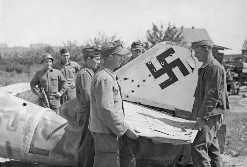 Немецкие пленные разбирают на лом реактивный истребитель Ме-262 (Messerschmitt Me 262). 
Район города Вюрцбург (Wurzburg), лето 1945 г. Позади слева двое 
американцев, наблюдающих за процессом.