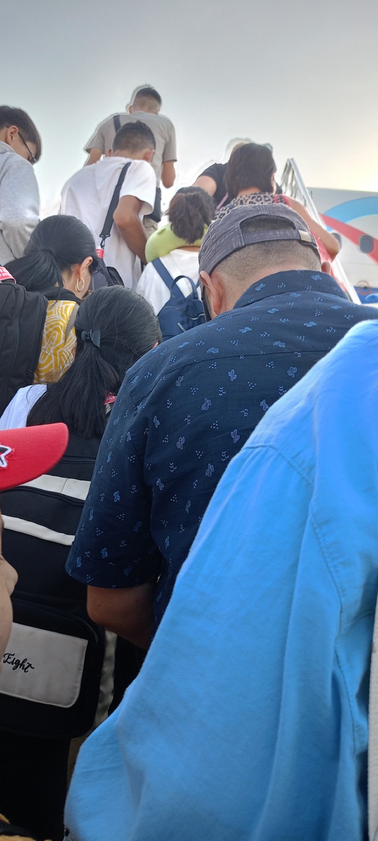 Очередь медленно движется вверх по трапу. Кто-то смотрит под ноги, кто-то — в небо. В каждом — своя история: кто-то летит домой, кто-то — в отпуск, кто-то оставляет за спиной целую жизнь.