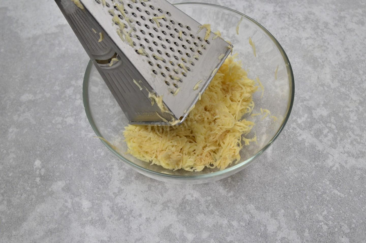 Картошку помойте и очистите. Натрите клубни на терке среднего размера. Немного отожмите ее, жидкость слейте.