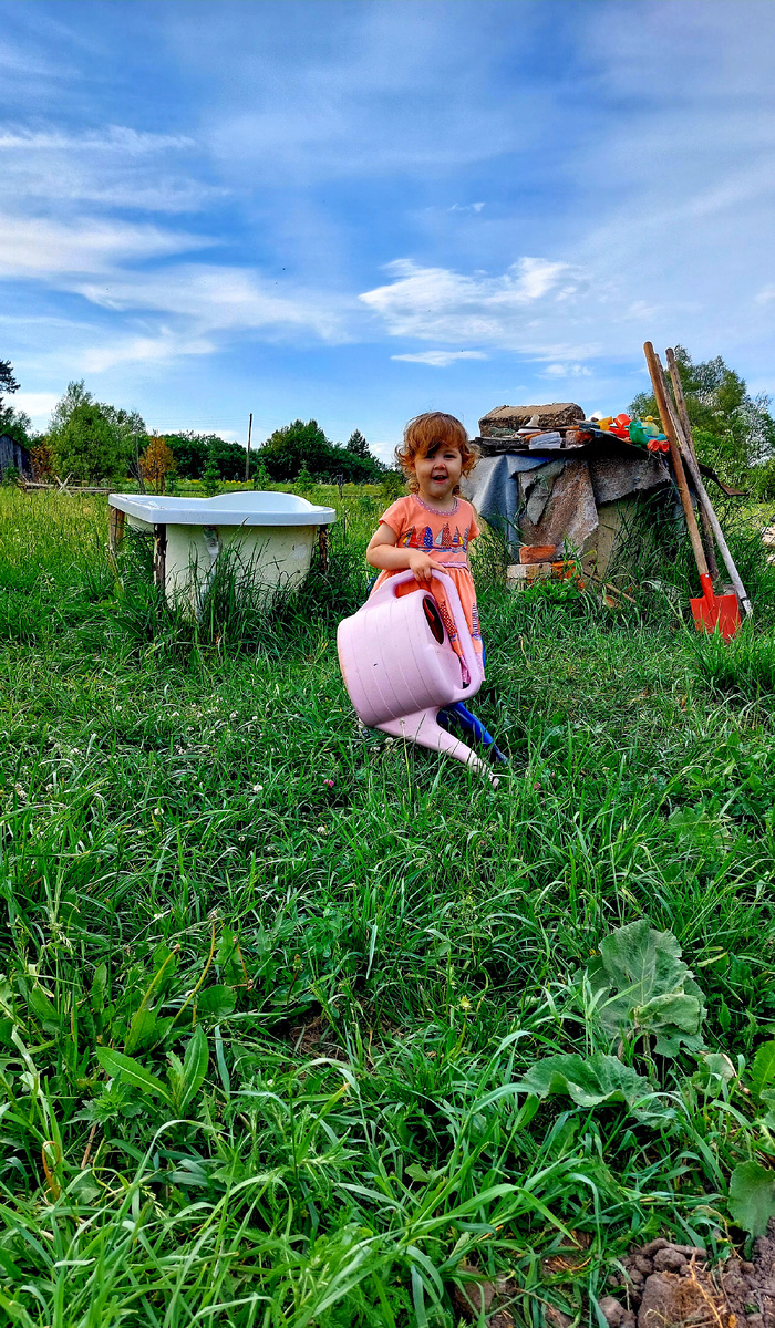 Маленькая дачница поливает с мамой огород