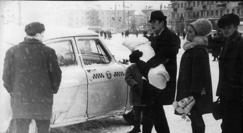 Магазин «Ткани» находится на Волковской улице, 9, в Люберцах, Московская область, СССР.

 На фотографии, выполненной в чёрно-белой гамме, запечатлена заснеженная улица. В центре кадра — радостный отец, который забирает ребёнка из родильного дома. Рядом с ним стоит его жена, держа в руках цветы, которые она недавно подарила. Все они тепло одеты: на них шапки, пальто и шарфы.

На переднем плане можно увидеть мужчину, который держит на руках ребёнка, укутанного в одеяло. На заднем плане виднеется белое такси с характерным узором, который был типичен для советских автомобилей того времени.