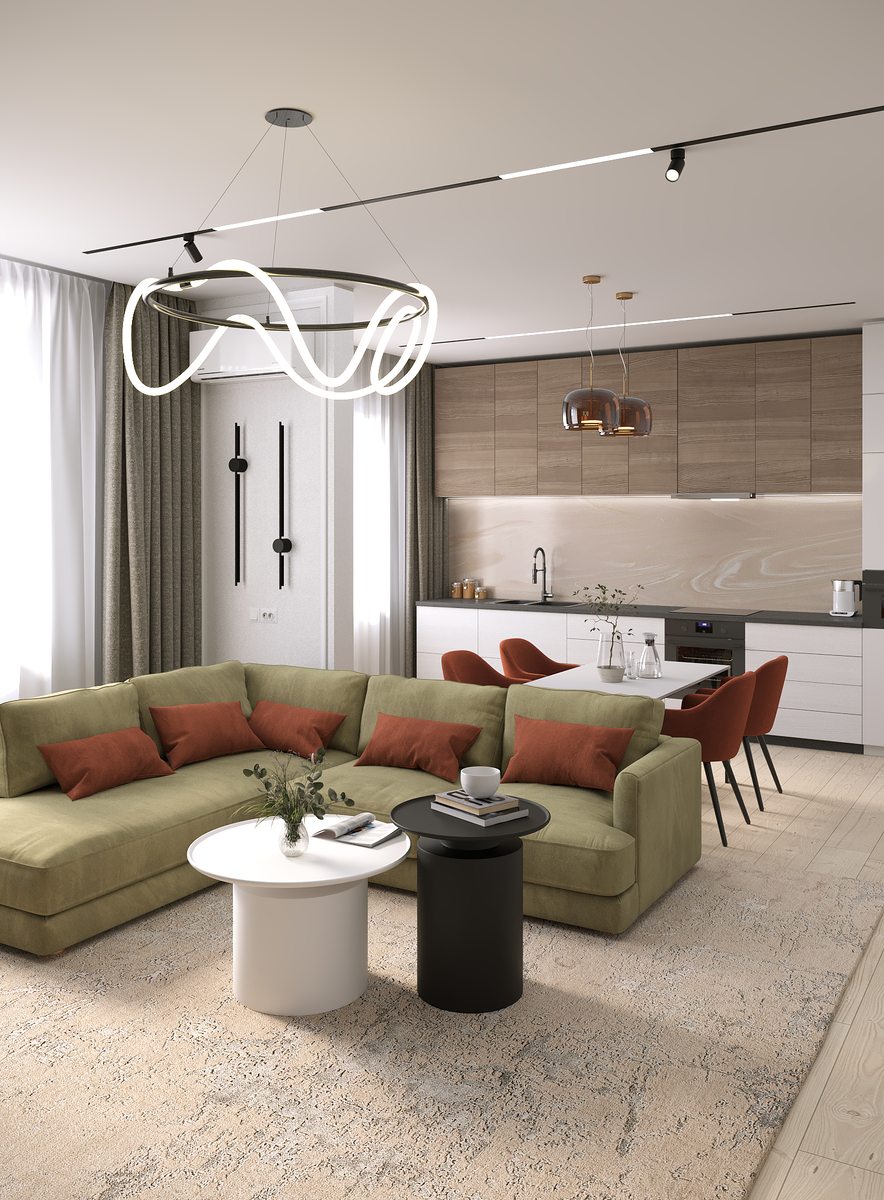 На изображении интерьер современной гостиной, объединенной с кухней. В центре гостиной расположен угловой диван оливкового цвета с декоративными подушками. Перед диваном стоят два небольших столика: круглый белый и цилиндрический черный. Над диваном висит современная люстра необычной формы. На заднем плане видна кухня с белыми шкафами и столешницей, а также стеновой панелью под камень. Над рабочей зоной кухни видны светильники. В комнате много естественного света, проникающего через большие окна с бежевыми шторами. Пол покрыт ковром с нейтральным узором. В целом, интерьер выглядит современным, стильным и уютным.