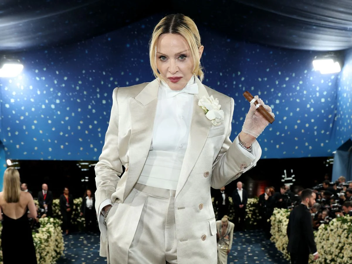 Мадонна в мае 2025 года на Met Gala, где она впервые за восемь лет появилась на красной дорожке. Она предстала в элегантном белом смокинге от Tom Ford, дополненном кружевными перчатками, бабочкой и бутоньеркой. Особое внимание привлек её аксессуар — зажжённая сигара, с которой она уверенно позировала перед камерами.