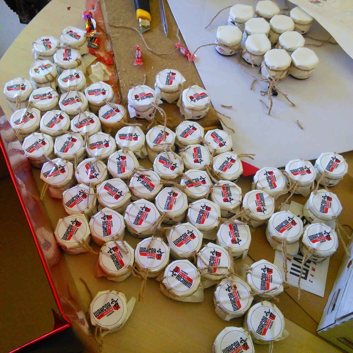 Малюсенькие баночки с вареньем, которые купили в супермаркете, сверху накрыли бумагой, перевязали бечёвкой и наклеили логотип компании