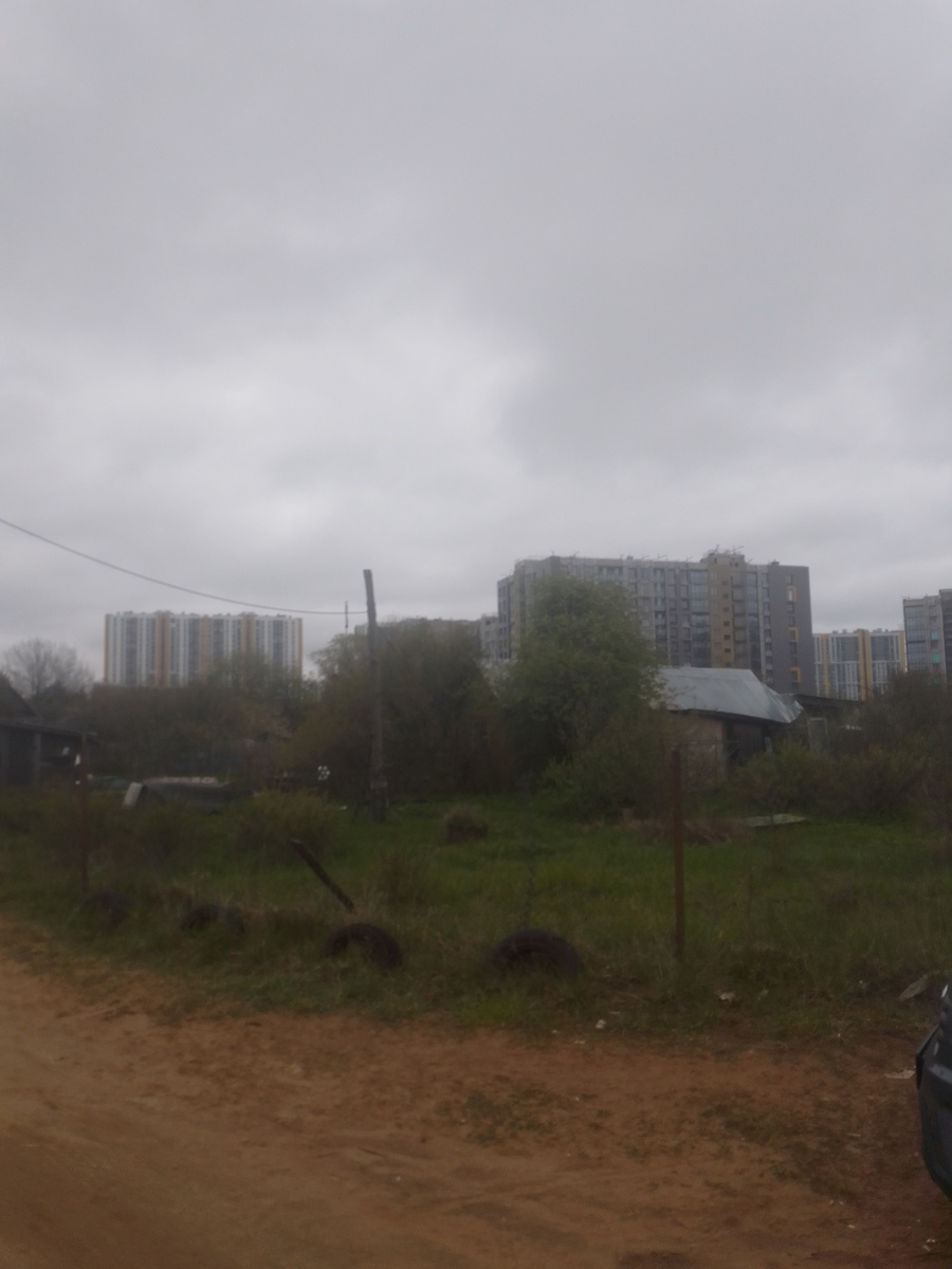 Грунтовая дорога, за ней старые дома, а не заднем плане высотки