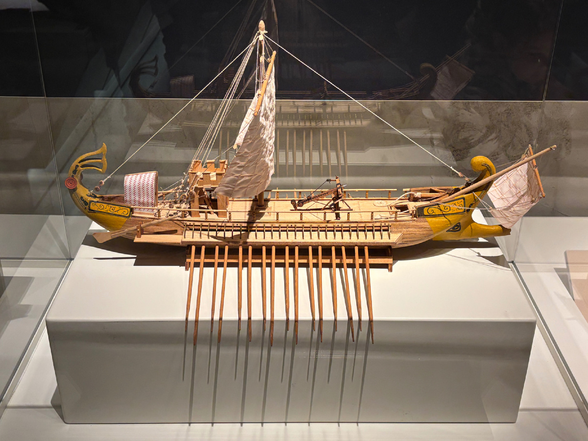 Трирема - древнегреческое гребное судно, которое использовалось в V-IV веках до н.э. Имело длину до 40 м и ширину до 6 м, а на борту могли работать до 170 гребцов. Трирема имела три ряда весел, что позволяло ей развивать высокую скорость и маневренность на воде. Триремы зачастую применялись в Средиземноморье, использовались в основном как военные суда, но и еще для торговли. Масштаб макета 1:20