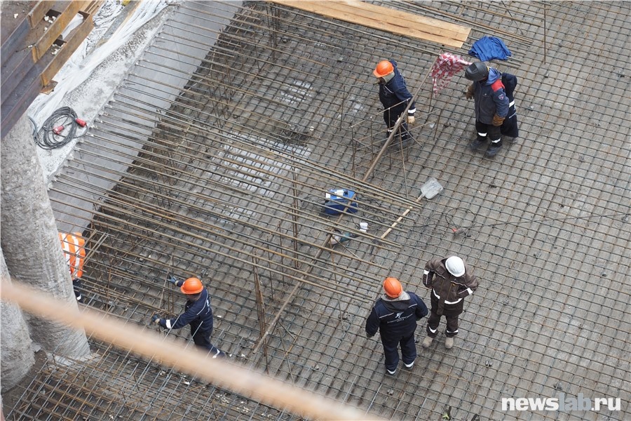 Внизу работают люди, создавая металлическую основу для железобетонной конструкции основания
