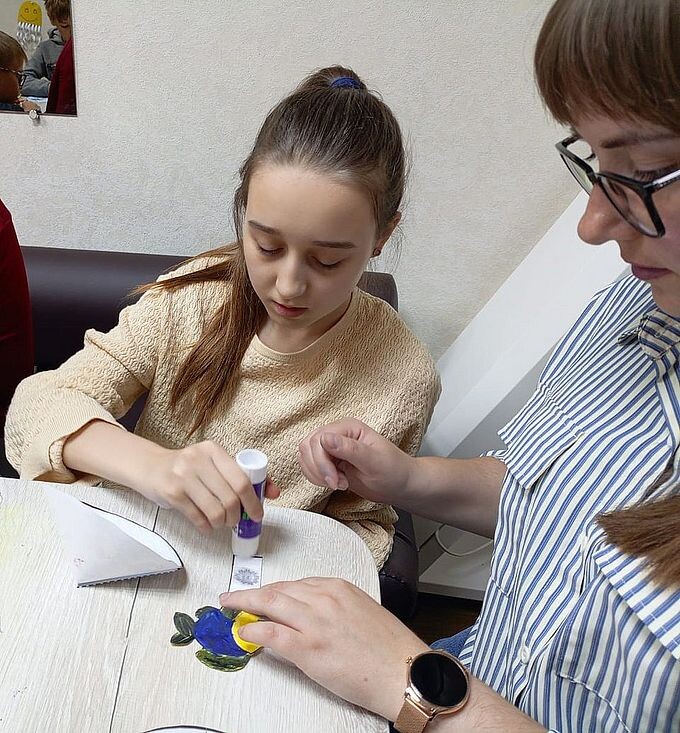 Першина Вероника Вячеславовна помогает девочке наклеить бумажную рыбку