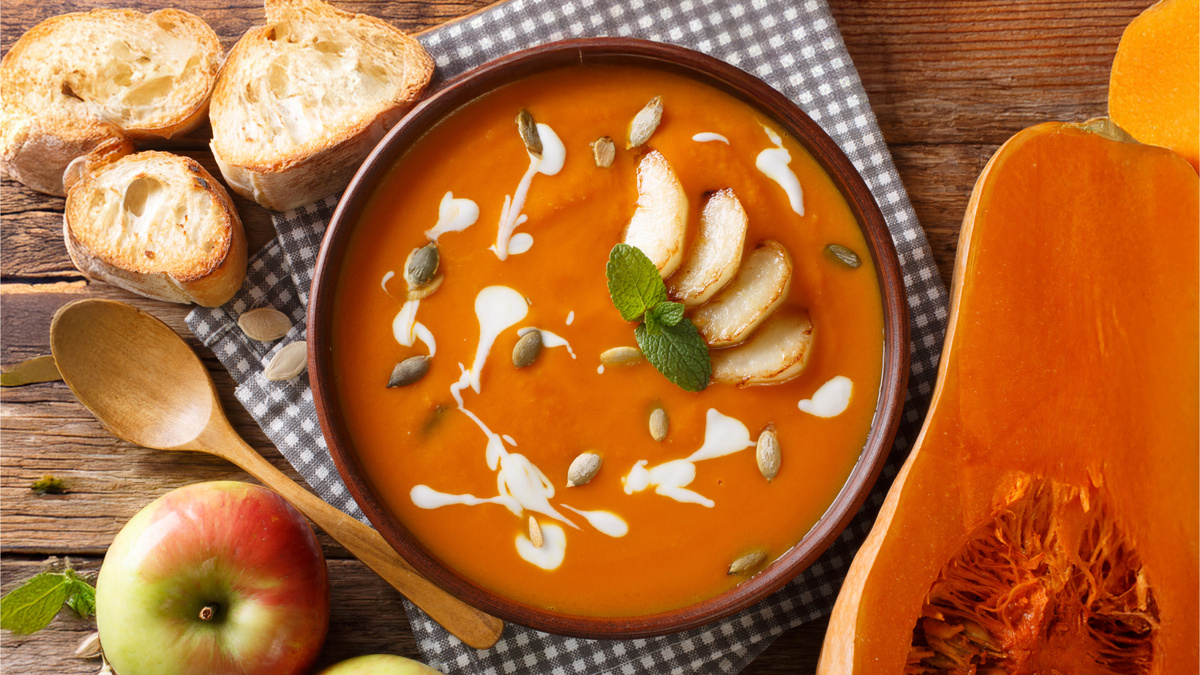 Густой тыквенный суп-пюре в тарелке, украшенный ломтиками яблок и каплей сливок. Рецепт сувид с сохранением витаминов.