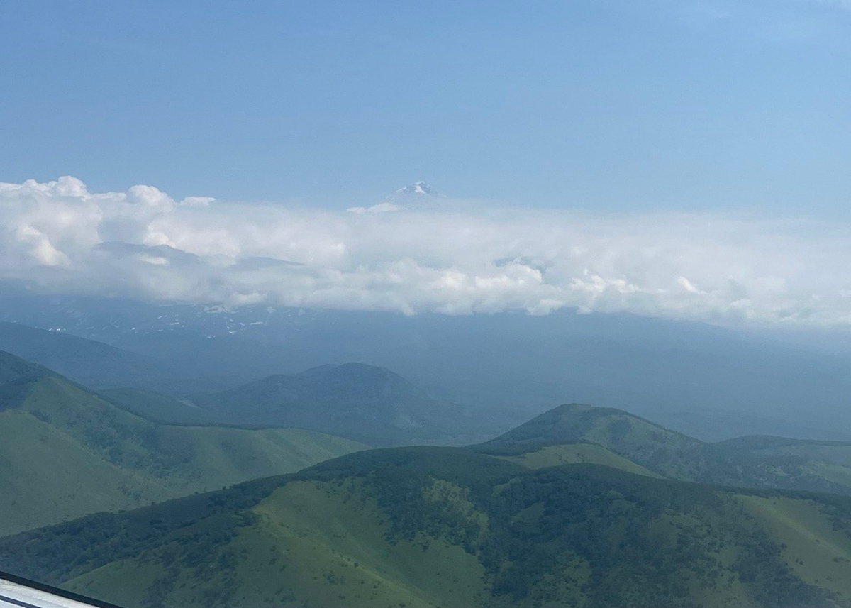 Над Камчаткой уже летим. Вдалеке виднеется вулкан среди облаков. (фото автора)