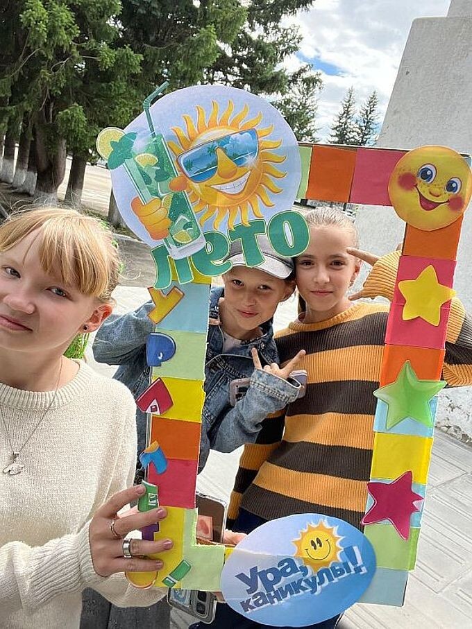 Три девочки фотографируются в рамке «Лето. Ура, каникулы!»
