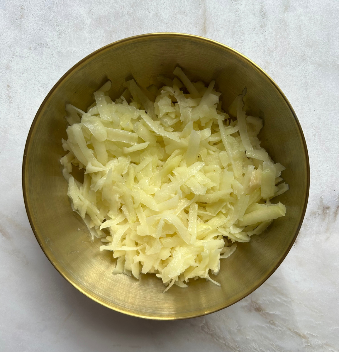 На крупной терке натереть картофелины.
Затем на 10 минут залить холодной водой.