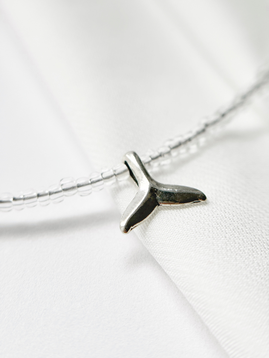 Прозрачный чешский бисер мерцает, словно капельки воды, а подвеска в виде серебряного китового хвоста с покрытием 925 пробы напоминает о свободе.