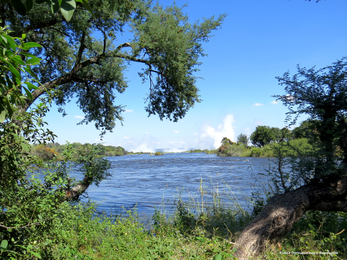 Река Замбези чуть выше падения. Видны столбы водяных брызг,поднимающиеся вверх от водопада.