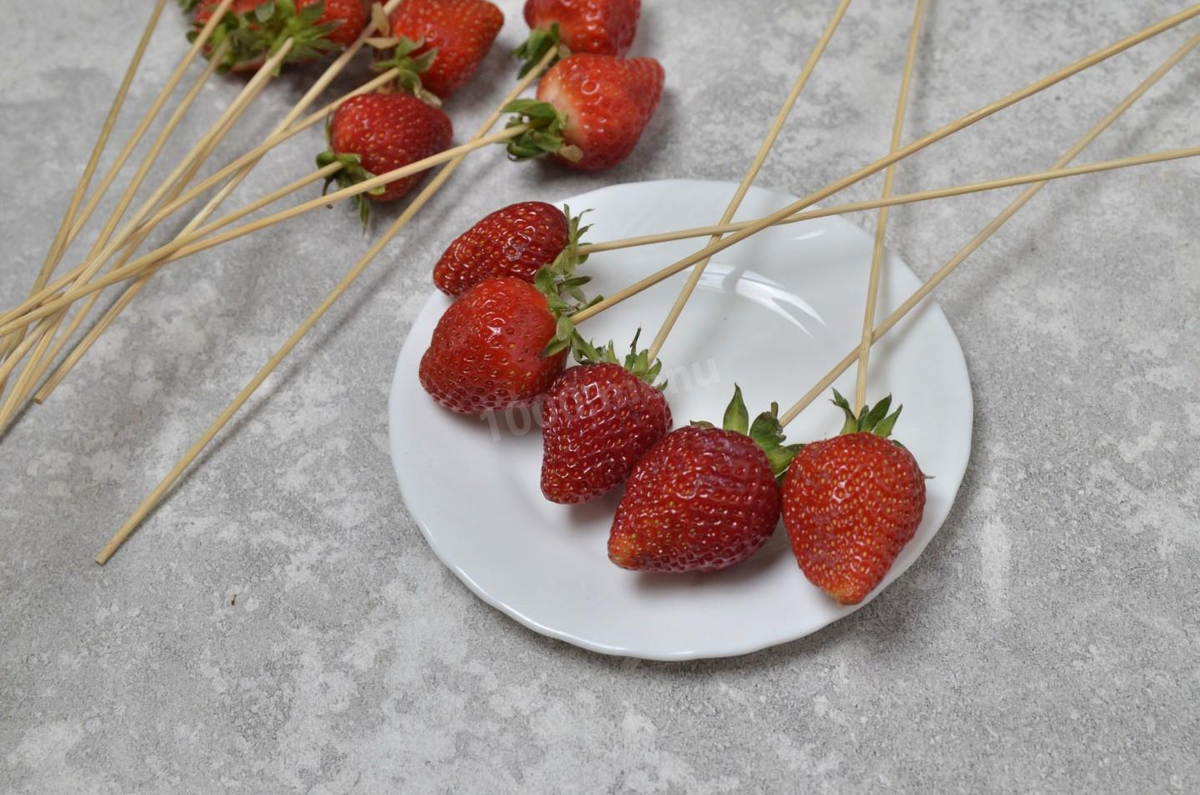 Клубнику промойте, а затем хорошо обсушите. Плодоножки, если они зеленые и свежие, удалять не нужно. Наколите каждую ягоду на длинную шпажку. Чтобы ягоды в дальнейшем не соскальзывали, предварительно можете обмакнуть кончик шпажки в растопленный шоколад.