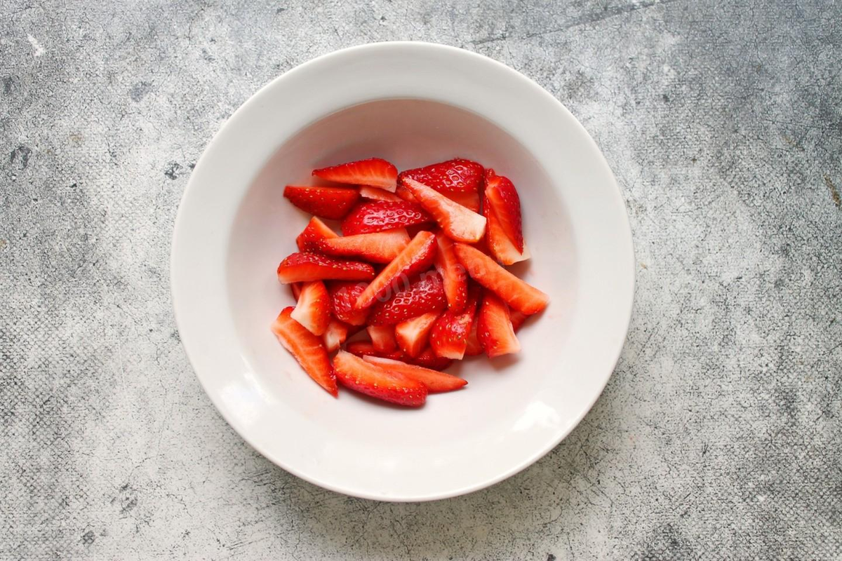 У клубники удалите зеленую плодоножку и разрежьте вдоль на 4-6 частей. Нарезка зависит от размера ягод. Положите клубнику в чашку.