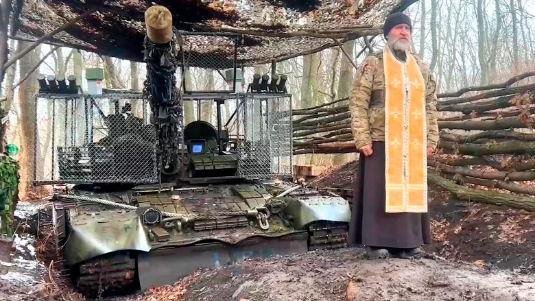 1. Танк с дополнительной защитой на замаскированной стоянке, и священнослужитель, проповедующий бойцам (кадр: RT)