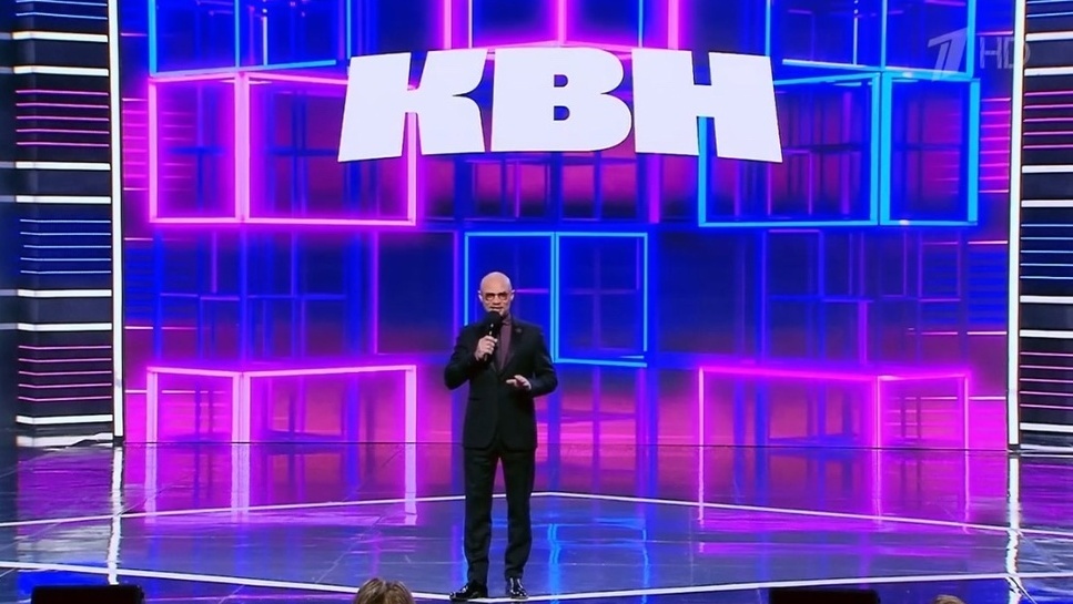 Респектабальный ведущий на сцене. Фото скрин шот. 