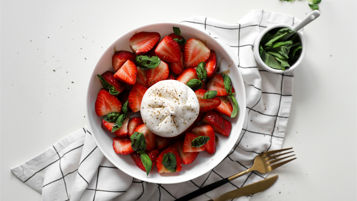 Простой летний салат: разрезанная клубника, шарик бурраты, базилик, заправка из бальзамика и оливкового масла.