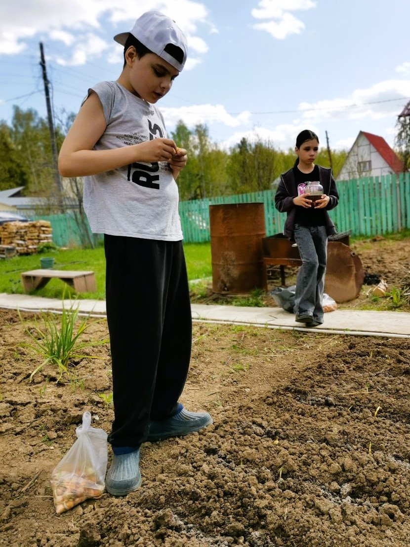 Роберт и сестра Рената в саду у бабушки. Учатся высаживать растения на грядках 