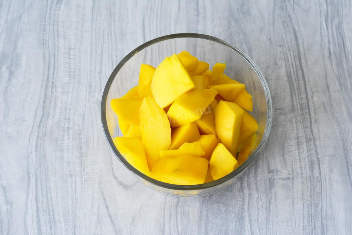 Манго вымойте, обсушите. Разрежьте плод пополам и удалите косточку. Каждую половинку очистите от кожуры и нарежьте кусочками. Важно очищать манго именно в такой последовательности. Ведь после снятия кожуры плод становится скользким. При разрезании его пополам можете порезаться. Косточка у манго крупная и плоская, мякоть плотно с ней срастается, поэтому придется повозиться. Как выбрать спелый сладкий манго читайте в конце рецепта.