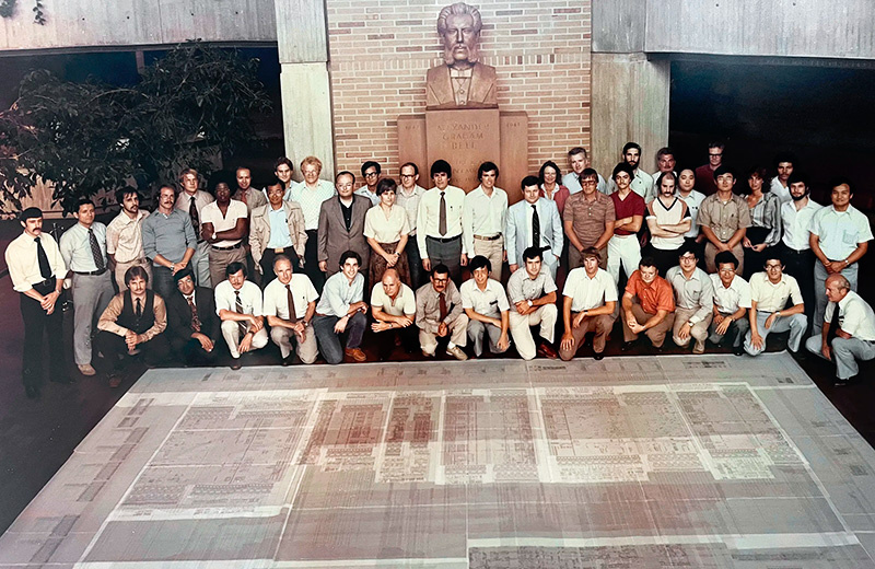 Члены команды Bellmac-32 из Bell Labs позируют рядом с гигантской принципиальной схемой чипа