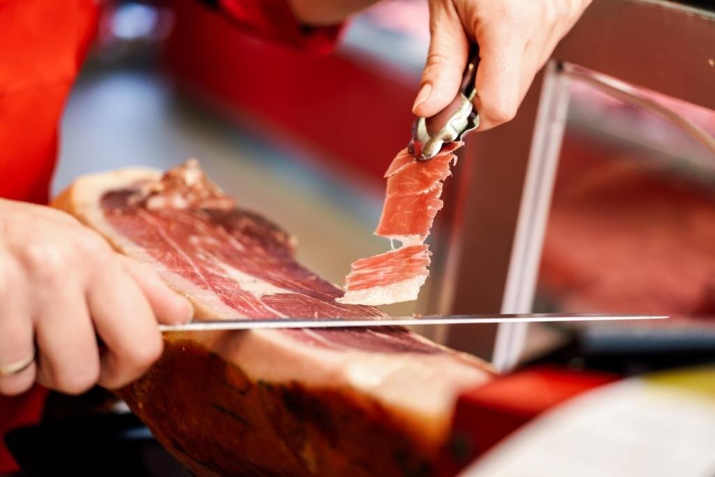    Professional cutter carving slices from a whole bone-in serrano ham Галина Ященко