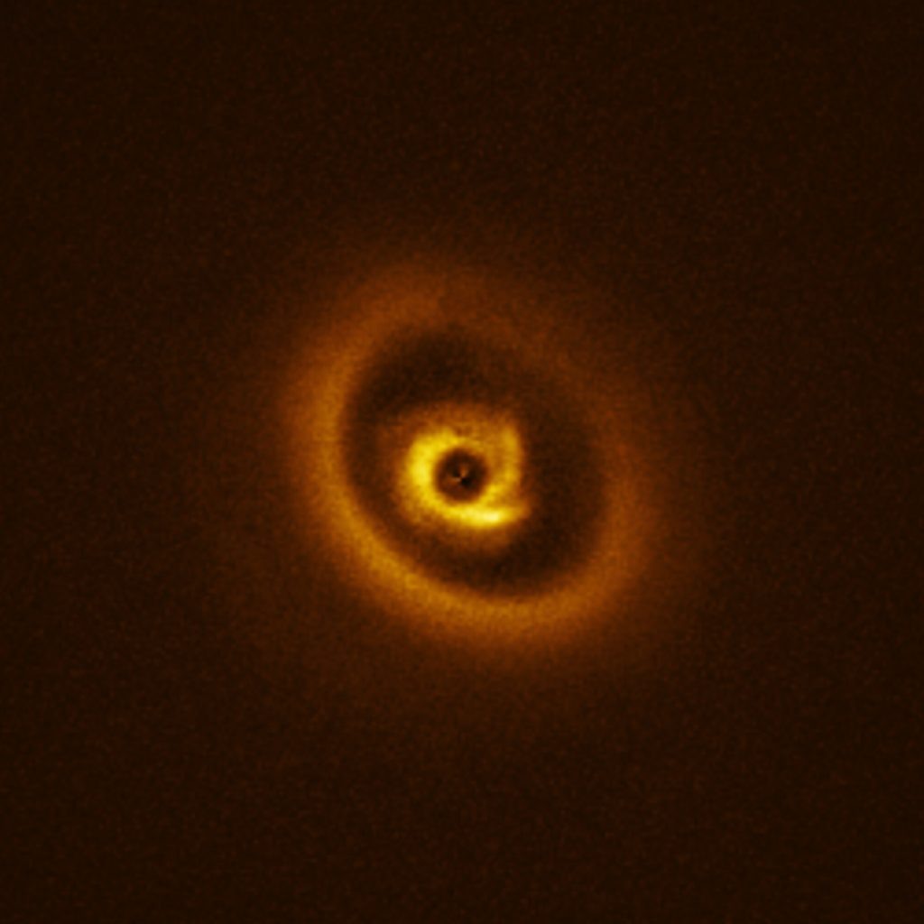    Astronomers may have caught a still-forming planet on camera, hidden somewhere in this stellar snapshot. Today’s Picture of the Week is a close-up of the star RIK 113, seen here surrounded by a cloud of gas and dust called a protoplanetary disc. These discs are a common feature around young stars, containing all the building blocks needed to make a new planet. Over time, these dusty discs will fragment and condense under the influence of gravity, forming larger objects like protoplanets. These planetary embryos carve out gaps in the dust around them, forming the intricate, ring-like structures that we can see in this disc.  The true complexity of this protoplanetary disc was first uncovered by the Atacama Large Millimeter/submillimeter Array (ALMA) in a study published last year. These results showed the presence of a gap, which hinted at a planet-like object embedded within it. This prompted another team of astronomers, led by Christian Ginski at the University of Galway, Ireland, to follow up with observations from ESO’s Very Large Telescope (VLT). Using the SPHERE instrument they found that the inner ring has intriguing spiral features. A detailed analysis of the data uncovered not just one, but two potential signals from planets around RIK 113, not far from the original detection with ALMA. For now, these signals are still more of a suggestion than a direct confirmation. However, with two separate studies from both ALMA and the VLT indicating the presence of at least one planet, these results are extremely promising for a future discovery. Link Research paper, accepted for publication in Astronomy & Astrophysics Александр Шереметьев