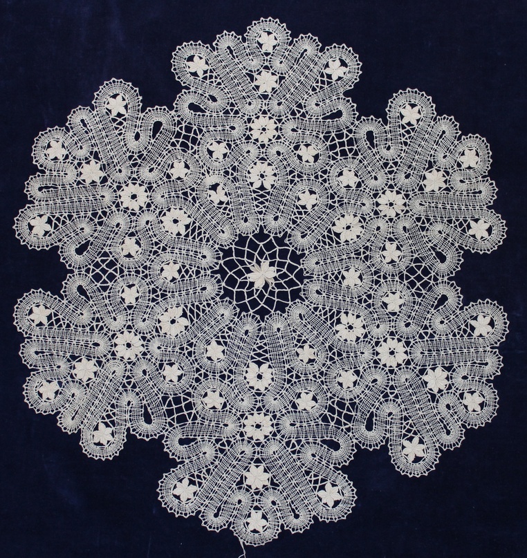 ККМ КП – 2651. Салфетка кремового цвета, с узорчатым краем. Салфетка напоминает цветок с 6 лепестками. Лепестки образуются из вилюшки, в центре которой - звёздочки из насновок. В центре салфетки - звёздочка из 12 насновок и решётка. Диаметр - 53 см. 1995 год. Автор – Е.С.Махова.