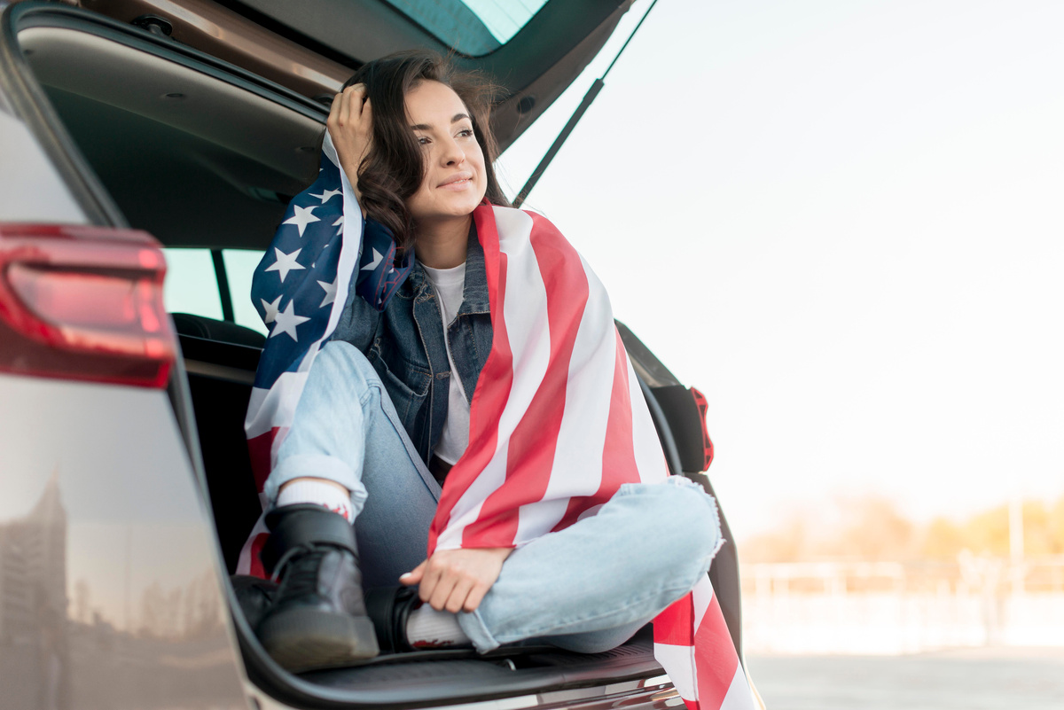 Источник изображения: freepik.com/free-photo/young-woman-holding-big-usa-flag-car-trunk_7968583.htm