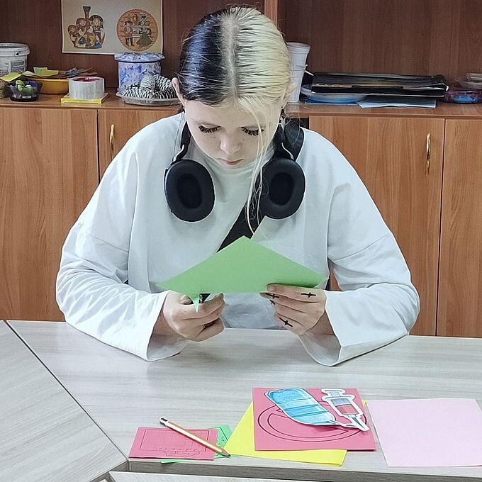 Девочка-подросток вырезает из бумаги фрагменты для стенгазеты