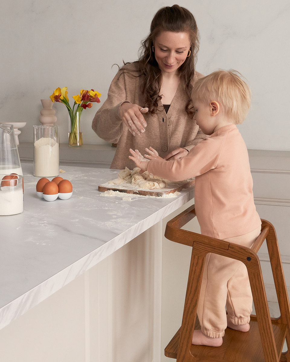 Малыш увлеченно помогает маме, стоя на башне помощника mommy's uma из массива дуба, когда она готовит! 