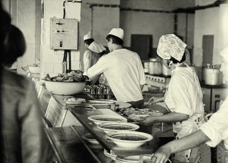 Когда в 1918 году к власти пришли большевики, они начали уничтожать всё, что ассоциировалось с «буржуазным прошлым». Под раздачу попали рестораны, трактиры и кафе — их закрывали как пережиток старого мира. Но людей нужно было кормить, причем быстро, дёшево и без лишних изысков. Так появился советский общепит — система общественного питания, которая на десятилетия определила гастрономические привычки миллионов граждан.