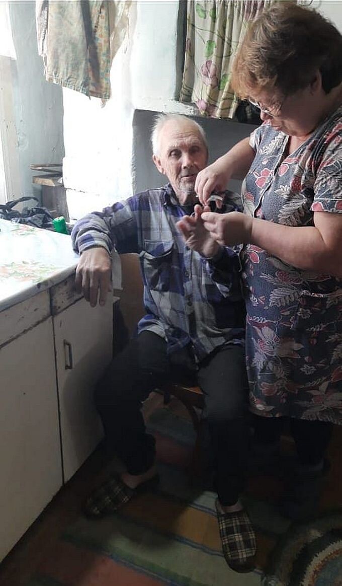 Социальная работница стрижёт ногти пожилому мужчине
